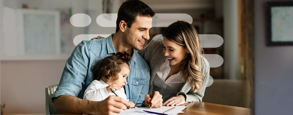 Um homem e uma mulher estão sentados à mesa com uma criança, sorrindo e interagindo em um ambiente familiar aconchegante, representando que o PLCA atende pessoas físicas com atenção independente do seu problema.